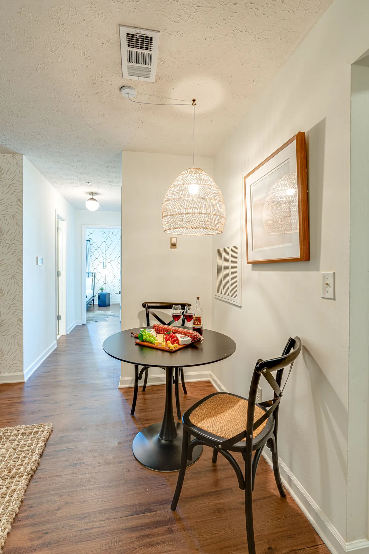 A close-up of the round black dining table accented by a woven pendant light above and a colorful food platter with wine glasses. The scene feels intimate and lively, evoking shared meals, casual chats, and the vibrancy of group gatherings.
