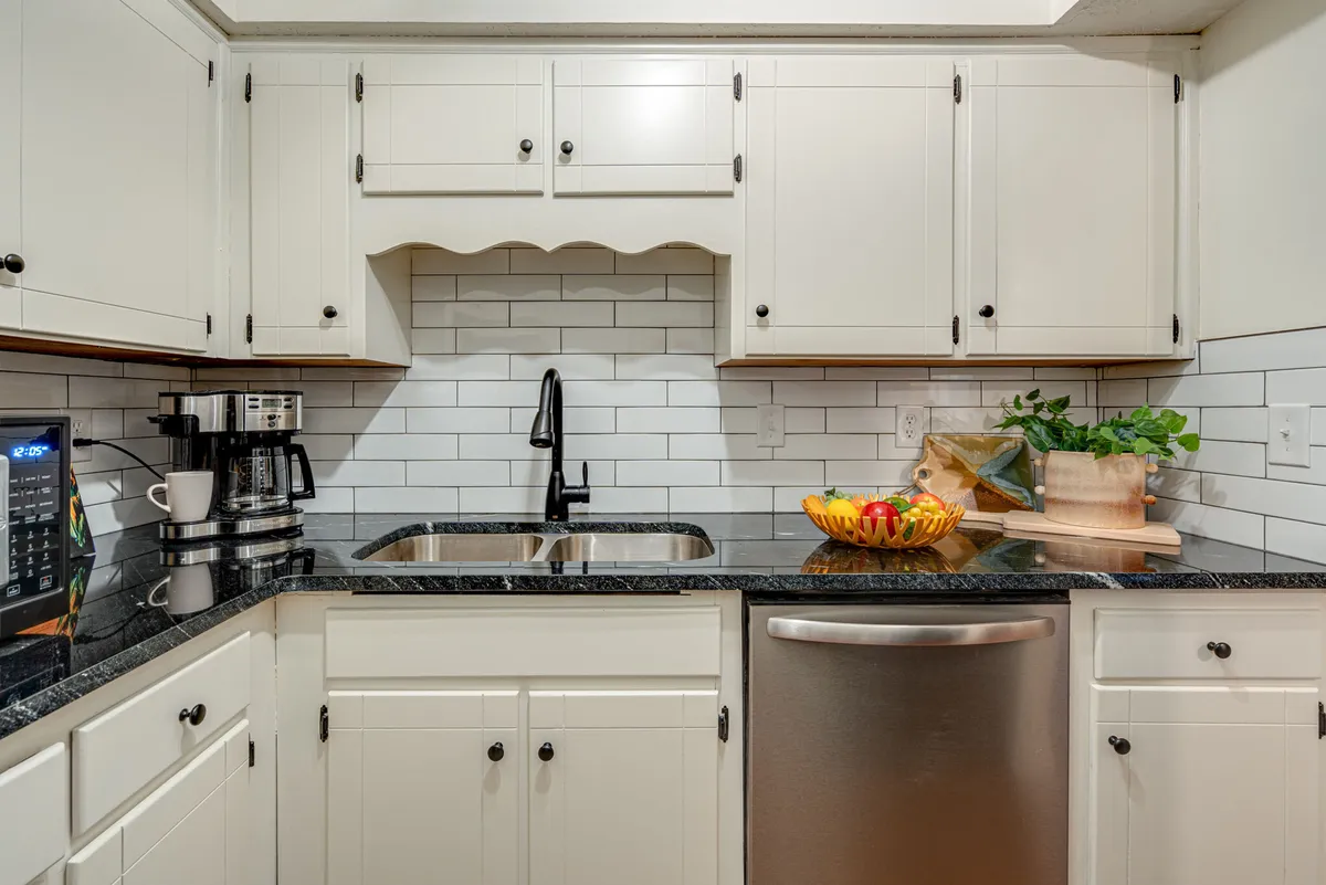 A contemporary kitchen scene with a black granite countertop, white subway tile backsplash, a modern black faucet, and a colorful fruit bowl. The space looks inviting and is ready for social cooking or morning coffee.