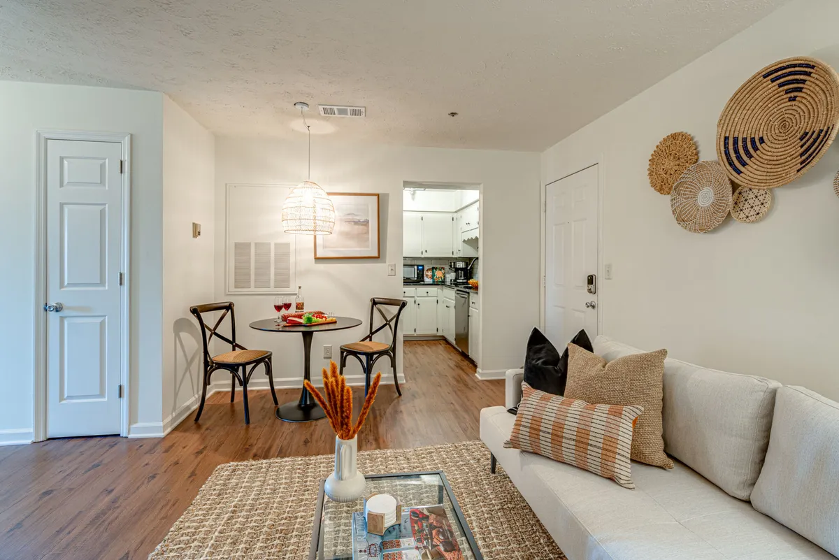 A wide view of the main living space, capturing the plush sectional sofa, a dining table set for casual meals or games, a glimpse into the kitchen, and decorative wall hangings that give the room a distinctive boho flair. The layout is open, welcoming, and designed for both relaxation and group gatherings.