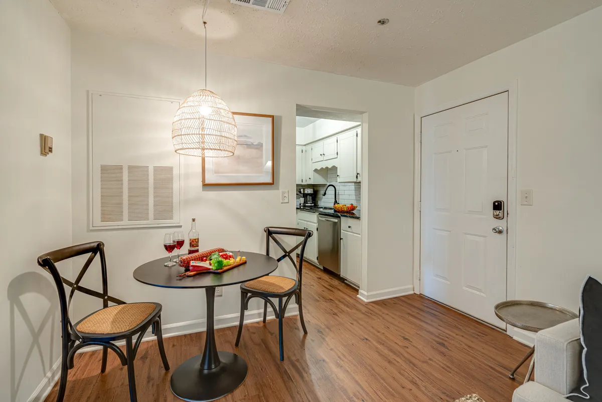 A cozy dining area featuring a round table set under a woven pendant light, with red wine glasses and a colorful spread of fruit and snacks. The atmosphere encourages intimate dining and relaxed conversations.